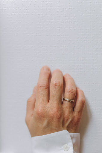 A person’s hand touches a sign with braille printed on it.