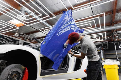 A man wrapping a white car door in blue vinyl 