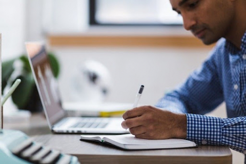 A man takes notes while working on the computer.