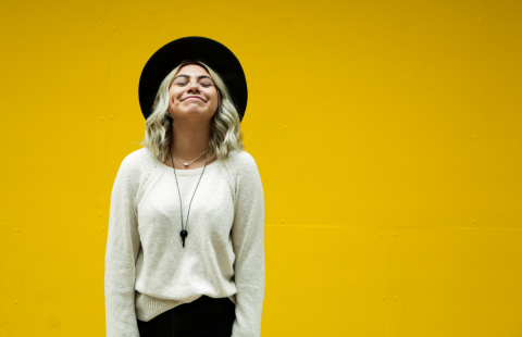 Smiling woman standing in front of a yellow wall.