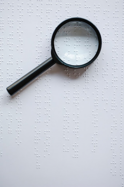 A magnifying glass sits on top of a sign printed with braille.