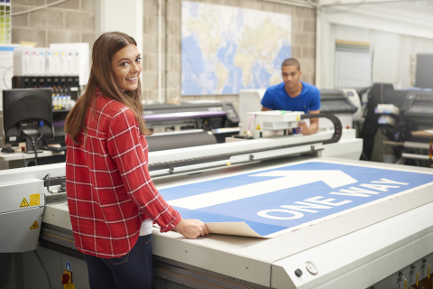 Print shop employees standing by a large format printer.