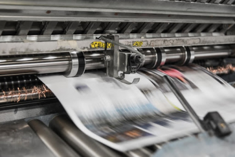 Copies of a newspaper shoot out of a large format printer.